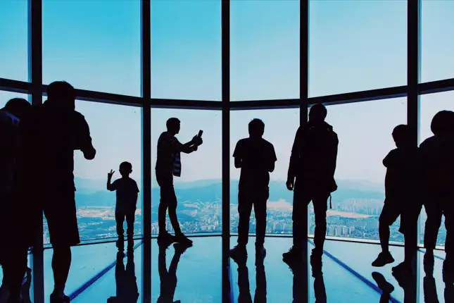Silhouette's of people looking out a glass view high up looking at city landscape