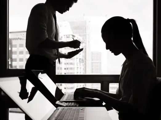 Silhouette's of two people working on a laptop