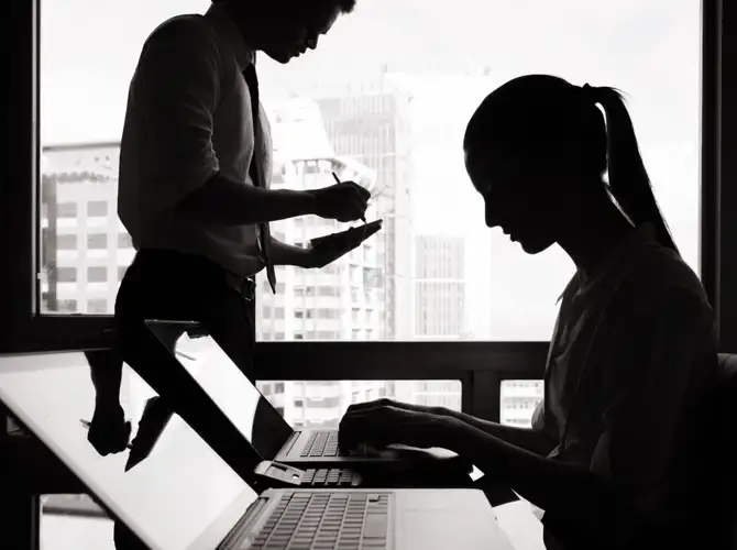 Silhouette's of two people working on a laptop