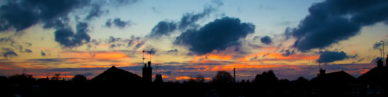 Houses in the skyline all dark with a colourful sky background made up of blue, orange and yellow